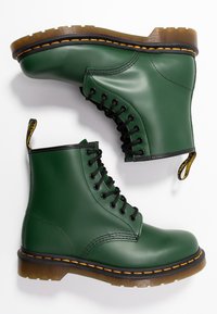 Green leather ankle boots with a glossy finish, black laces, yellow stitching, and a pull tab. Features a thick, ridged rubber sole.