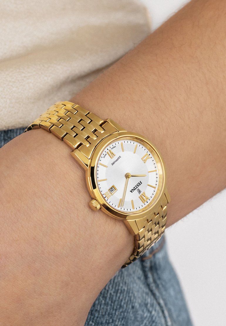 Gold metal wristwatch with a white dial, gold hour markers, date display at 6 o’clock, and a woven link band.