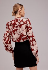 Czerwona kwiatowa bluzka z długim rękawem z beżowymi kwiatami, teksturowana czarna mini spódniczka, bufiaste rękawy oraz luźny krój z tyłu.