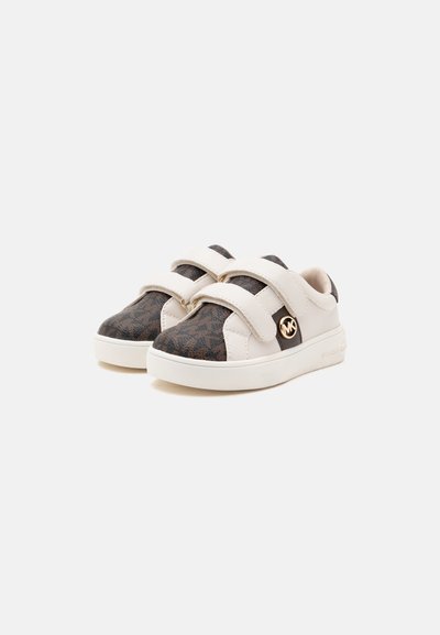 Ζευγάρι χαμηλά sneakers με καφέ υφασμάτινο σχέδιο, μπεζ δερμάτινα λουριά και λευκές σόλες, με χρυσλό στρογγυλό λογότυπο στο πλάι.