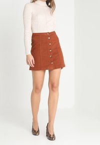 Rostfärgad denimkjol med rak skärning, med knappstängning fram och två sidofickor. Bärs med en krämfärgad långärmad top i ribbad struktur.