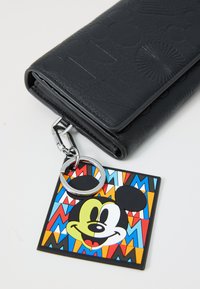 Portefeuille en cuir noir texturé avec un motif embossé, présentant un accent en métal argenté et une étiquette colorée de Mickey Mouse.