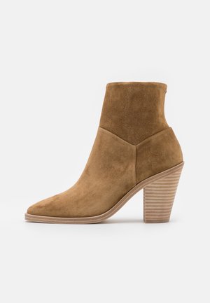 Bottine en suède marron avec un bout pointu, un tige effilée et un talon bloc strié. Présente une texture lisse et un design minimaliste.