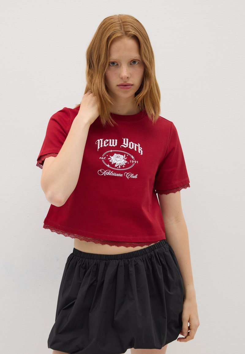 Camiseta roja corta con texto gráfico en blanco que presenta un diseño de rosa, con un borde de encaje en las mangas, combinada con una falda negra con recogido y elástico en la cintura.