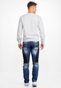 Grijze sweatshirt met lange mouwen, gecombineerd met blauwe spijkerbroeken met kontrasterende panelen en gestikte details, gedragen met witte sneakers.