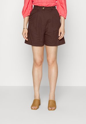 Shorts marron taille haute en coton avec des plis, dotés d'une fermeture à bouton sur le devant, associés à des mules en osier beige.