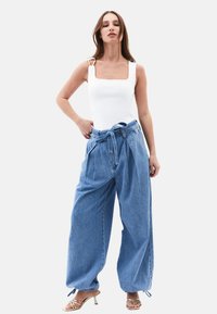 Body bianco a collo quadrato abbinato a pantaloni di jeans azzurri larghi con cintura annodata e tasche laterali. Sandali con tacco alto.