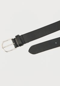 Sort læderbælte med en glat tekstur, sølvfarvet metalklemme og en spids ende. Har fem huller til justerbar størrelse.