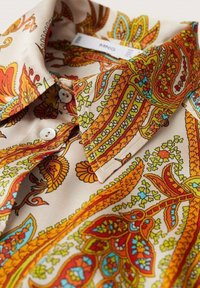 Chemise à col avec un motif floral paisley orange, jaune, rouge et bleu sur un tissu beige, dotée de boutons blancs et d'un col replié.