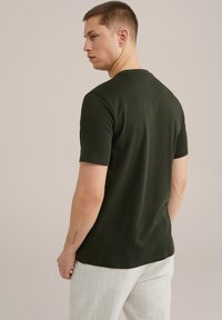 Temna zelena majica s kratkimi rokavi iz mehke tkanine, ki ima okroglo ovratnico in sproščen kroj. Nosi se z svetlimi, črtastimi hlačami.