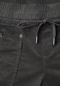 Close-up of dark gray corduroy pants with elastic waistband, front pocket with metal rivets, and braided drawstring tied in a bow with metal tips.