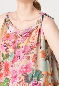 Top con estampado floral que presenta una tela ligera y transparente con flores vibrantes en rosa, naranja y verde. Cuello deshilachado y acampanado con tirantes ajustables.