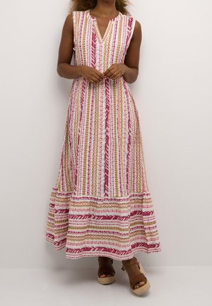 Vrouw draagt een mouwloze, enkellange jurk met verticale roze, rode en beige strepen, gecombineerd met bruine sleehakken.