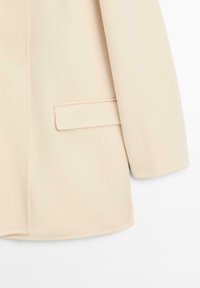 Lichtbeige op maat gemaakte mantel van zachte stof, met een enkele zak en strakke lijnen, een gladde textuur en modern snit.
