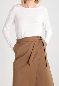 White long-sleeve top with a textured finish paired with a brown, wrap-style skirt featuring a tie at the waist. Smooth fabric with a flowing design.