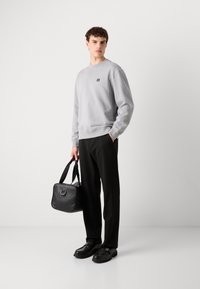 Sudadera gris con un pequeño logo bordado, pantalones negros holgados, zapatos negros pulidos y un bolso negro de hombro.
