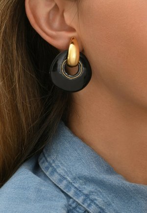Boucles d'oreilles circulaires dorées et noires avec une finition noire brillante, présentant un anneau central doré et des accents texturés.