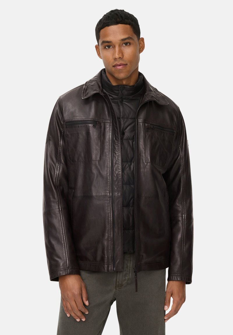 Bruine leren jas met een kraagontwerp, twee borstzakken en een rits. Het interieur heeft een gewatteerde zwarte voering voor extra warmte.