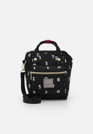 Bolso de tela negra con patrones de números blancos, bolsillo frontal con cremallera, asas superiores con correa roja y una correa de hombro desmontable.