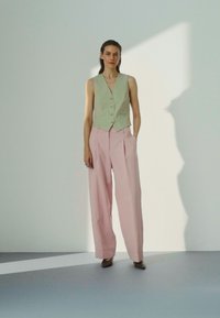 Lys grønn vest med knapper, tilpasset og kombinert med høyhalsede, vide rosa bukser. Glatte teksturer, minimalistisk design og skreddersydd passform.