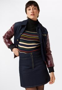 Navy wool jacket with burgundy vinyl sleeves, featuring gold embroidery. Underneath, a striped ribbed turtleneck and a denim skirt with a zipper.