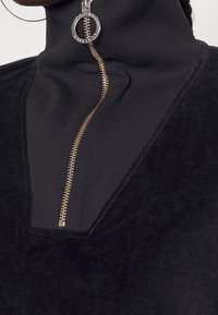 Maglione zip-up nero con colletto alto, caratterizzato da una texture a coste e da una cerniera metallica con un anello come tirante.