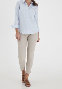 Jasnoniebieska koszula zapinana na guziki z długimi rękawami, podwiniętymi na mankietach, zestawiona z beżowymi wąskimi spodniami i brązowymi sandałami na paski.