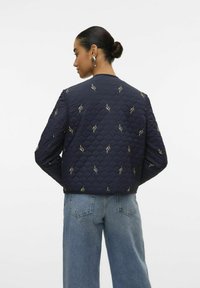 Mornarica prešita jakna z vezenjem z zlatimi listi, lahka zasnova, rebrasti manšeti in spodnji del. Nosi se z visokim pasom lahkimi jeans hlačami.