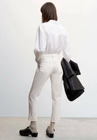 Jeans blancs taille haute, coupe droite avec poches arrière, associés à une chemise blanche à boutons et une veste en cuir noire, portés avec des sabots.