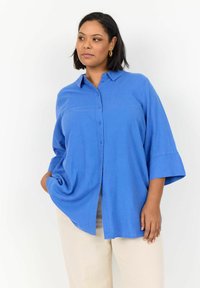 Camisa azul de botones con cuello, mangas de ¾, corte holgado y detalle de abertura lateral, confeccionada en tela ligera.
