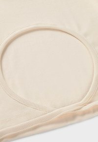 Gros plan de tissu beige côtelé avec une ouverture circulaire et des coutures renforcées le long des bords.