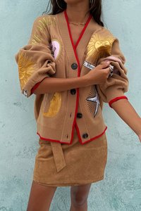 Tan strikket cardigan med rød kant, store knapper og forskjellige sol- og månedsymboler. Kombinert med en tan skinn mini nederdel.