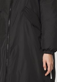 Černá péřová bunda s předním zipem, pružnými manžetami a boční kapsou. Hladká textura s označením na lemu.