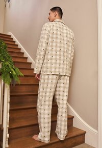 Beige kostkovaný pyžamový set s malými zelenými vzory stromů, s button-up vrškem a volnými kalhotami. Hladká tkanina, uvolněný design.