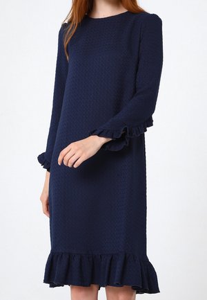 Marineblaues Kleid mit strukturiertem Muster, langen Ärmeln und rüschierten Manschetten sowie Saum. Schlichtes, knielanges Design ohne zusätzliche Akzente.