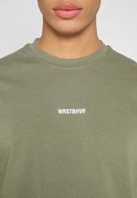 Olivově zelené bavlněné tričko s kulatým výstřihem a krátkými rukávy, na hrudi se bílým vyšitým logem "WRSTBHV".