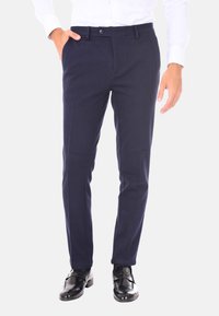 Pantaloni tailored blu navy con frontale piatto, tasche laterali e chiusura con bottone, realizzati in tessuto leggero, abbinati a scarpe eleganti nere.