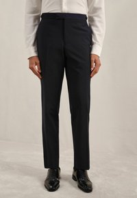 Pantaloni de costum navy dintr-un material neted, cu o croială ajustată, față netedă și detalii cu nasturi la talie. Pantofi: din piele neagră, lustruiți.
