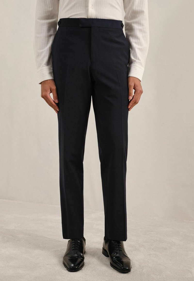 Pantaloni de costum navy dintr-un material neted, cu o croială ajustată, față netedă și detalii cu nasturi la talie. Pantofi: din piele neagră, lustruiți.