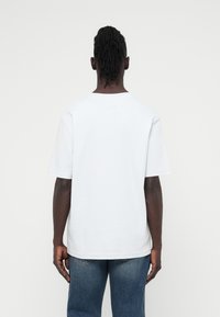 Λευκό βαμβακερό κοντομάνικο μπλουζάκι με κλασικό στρογγυλό λαιμό, χαλαρή εφαρμογή και λεία υφή, εμφανιζόμενο από πίσω.