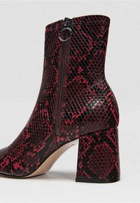 Bottine à imprimé serpent rouge et noir avec un talon carré, une fermeture éclair latérale et une texture lisse. Présente un design structuré et une finition brillante.