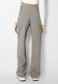 Grijze, op maat gemaakte broek met een wijd uitlopende pijp en een gladde textuur. Voorzien van een mid-rise tailleband en subtiele zijzakken.