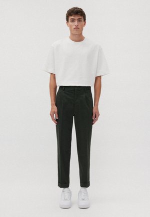 Hvid kortærmet t-shirt parret med mørkegrønne skræddersyede bukser, der har en afslappet pasform og opkrøllede ærmer, suppleret af hvide sneakers.