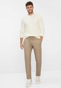 Crème gebreide trui met een ronde halslijn, gecombineerd met lichtbruine joggers met een elastische tailleband en zijzakken. Witte sneakers.