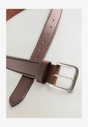 Brūns ādas jostasizs, kas aprīkots ar sudraba metāla sprādzi, ar redzamām šuvēm gar malām un vairākām caurumiem izmēra regulēšanai.