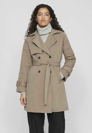 Abrigo beige de trench con botones de doble pecho, cintura ceñida con cinturón, bolsillos en ángulo y amplios solapas, superpuesto a un suéter de cuello alto gris.