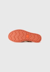 Skoens såle har et zigzag mønster i oransje gummi, med en teksturert overflate for grep og forsterkede kanter for holdbarhet.