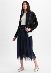 Zwarte satijnen bomberjack over een lichtgrijze top, marineblauwe tulle midi-rok, zilveren slingback flats en een kleine zilveren clutch.