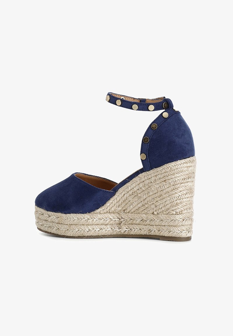 Marineblauwe suède espadrille-wedged met jutezool, enkelbandje met gouden studs, ronde neus en textuur van touwdetails op de wedge.