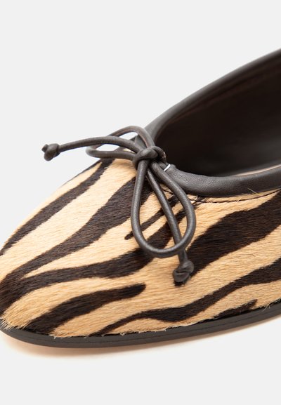Πλακέ παπούτσι με επάνω μέρος από μαύρο και μπεζ γούνινο ύφασμα με σχέδιο ζέβρας και μαύρο δερμάτινο φιόγκο στην κορυφή.